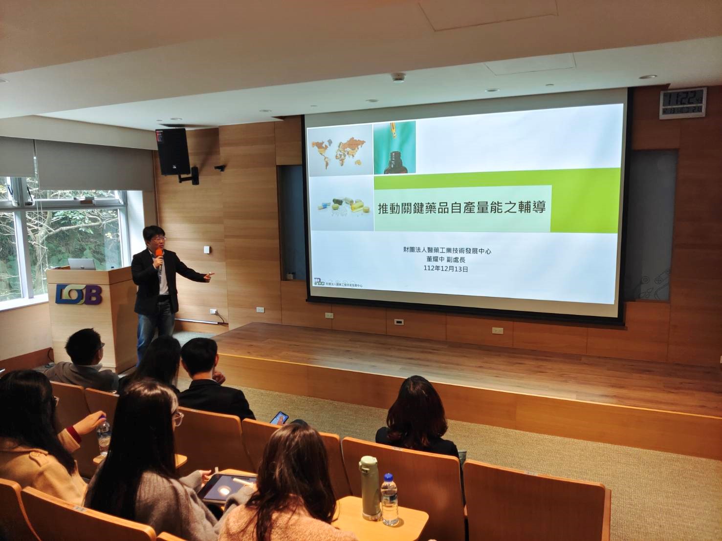 這張圖片顯示一位演講者在教室前方進行簡報。 